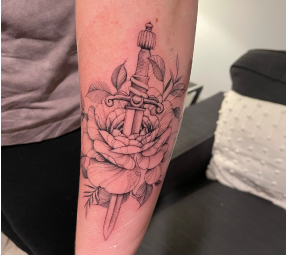 Fine line tattoo of a peony flower with a dagger going through the flower